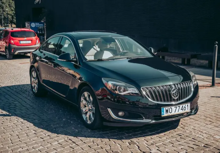 Elegancki, ciemnozielony Buick Regal z chromowanymi felgami stoi na brukowanej ulicy.