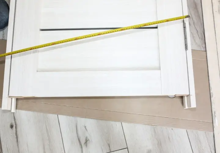 Białe drzwi z widoczną miarką. Mierzone skrzydło drzwiowe ma szerokość ok. 70 cm, co sugeruje jaki otwór na drzwi 70 będzie potrzebny.