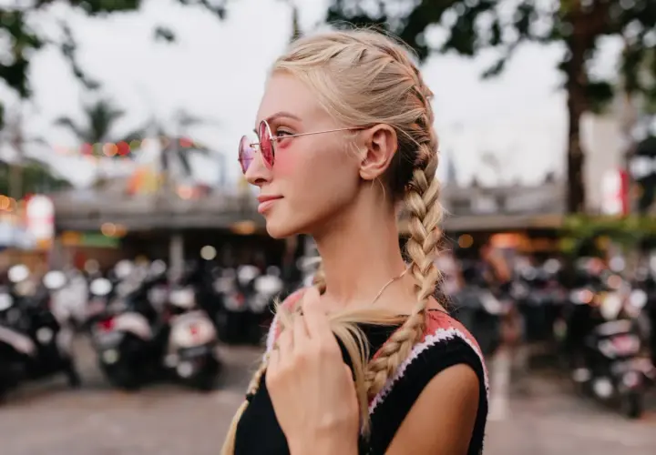 Blondynka w okularach przeciwsłonecznych z dwoma warkoczami na tle skuterów.