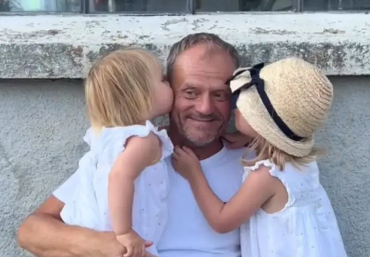 Donald Tusk z dwiema córkami całującymi go w policzki.