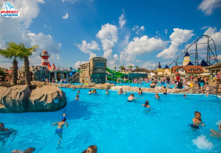 Energylandia strefa wodna tętni życiem. Ludzie kąpią się w basenie, bawią na zjeżdżalniach, a w tle widać rollercoaster.