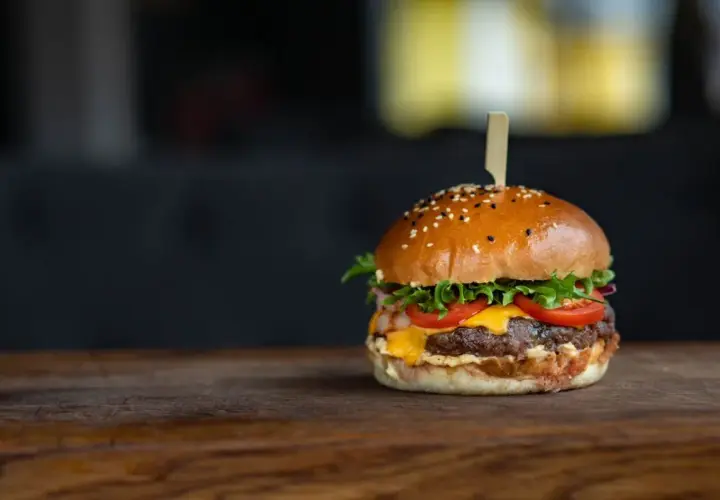 Apetyczny hamburger z serem, pomidorami i sałatą na drewnianym blacie.