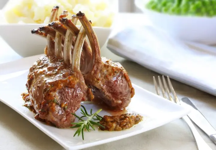 Un délicieux carré d'agneau rôti, nappé d'une sauce savoureuse, est servi avec une branche de romarin.