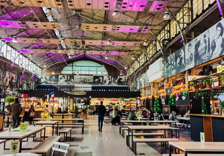Wegańskie restauracje Warszawa w hali targowej z neonami i czarno-białymi zdjęciami na ścianach. Wiele stolików i ław, ludzie jedzą i spacerują.