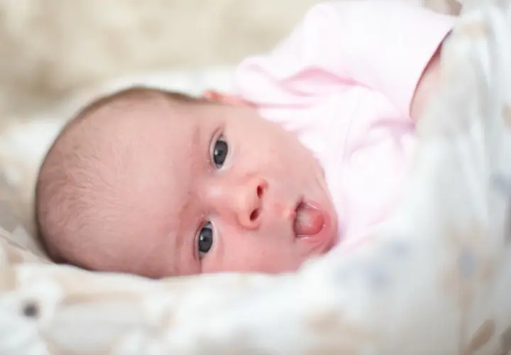 Neonato con lingua bianca, vestito di rosa, guarda incuriosito.