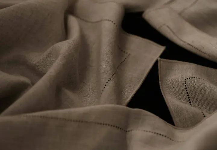 Draped linen fabric, perfect for breathable summer pants, features delicate dotted stitching along its edges.