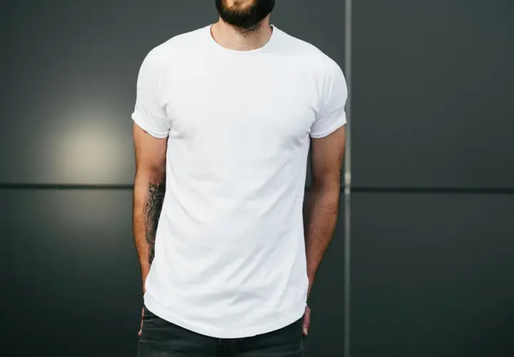 Mann mit Bart trägt weißes T-Shirt und Jeans, Hände in den Taschen.