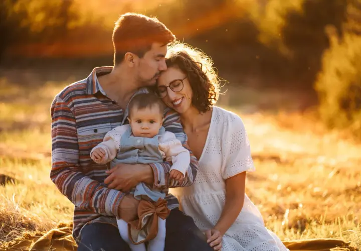 Piękne zdjecia rodzinne w złotym świetle zachodzącego słońca. Tata obejmuje córeczkę, mama wtula się w tatę.