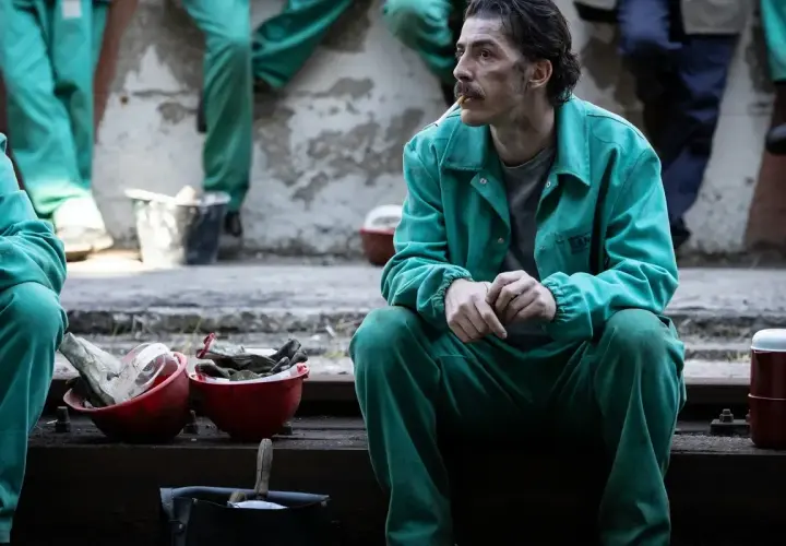 Uomo con baffi, in tuta verde, fuma una sigaretta. Le sue mani sono giunte, sembra pensieroso. Le recensioni per la palazzina LAF potrebbero essere simili.
