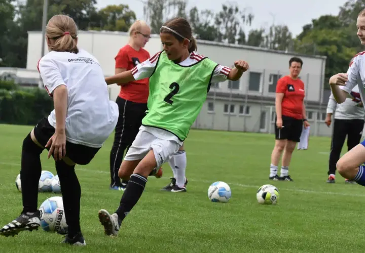 Mädchen im **Jugend Fußball** Training üben Dribblings. Ein Mädchen mit grüner Weste und der Nummer 2 am Ball.