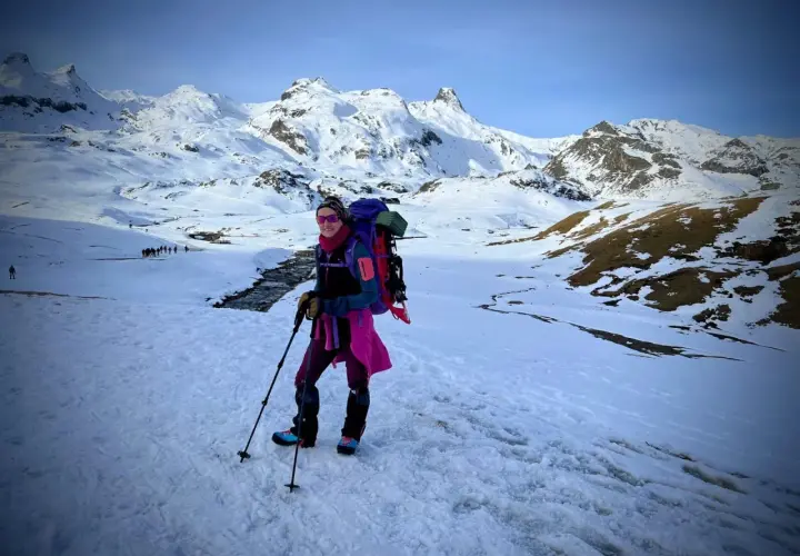 Una mujer con mochila y bastones disfruta de excursiones nieve en un paisaje montañoso cubierto de blanco.