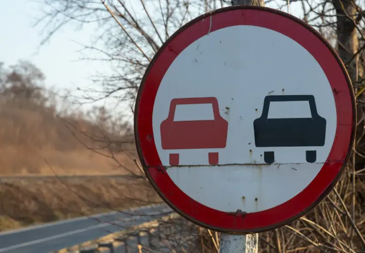 Znak drogowy zakaz wyprzedzania. Czerwony samochód z przodu, czarny z tyłu.