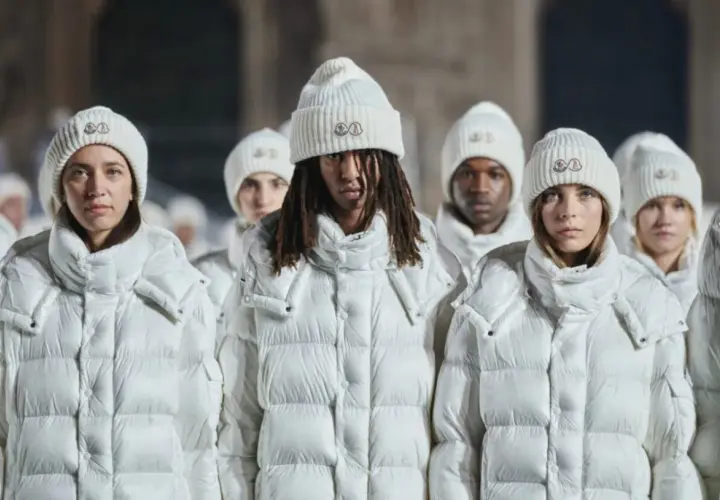 Grupa osób w białych kurtkach i czapkach Moncler. To właśnie moncler co to za firma – marka znana z luksusowej odzieży zimowej.