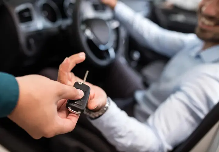 En person lämnar över bilnycklar till en leende man i förarsätet, redo för en ny resa eller kanske en avskrivning bil.