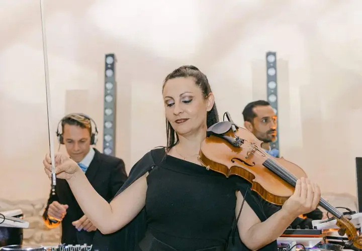 Une violoniste joue lors d'un mariage, avec des DJs en arrière-plan. Un prix DJ mariage pour une ambiance unique.