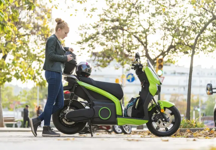 Mujer con casco y móvil junto a ciclomotor eléctrico verde. ¿Cuál será su velocidad máxima?