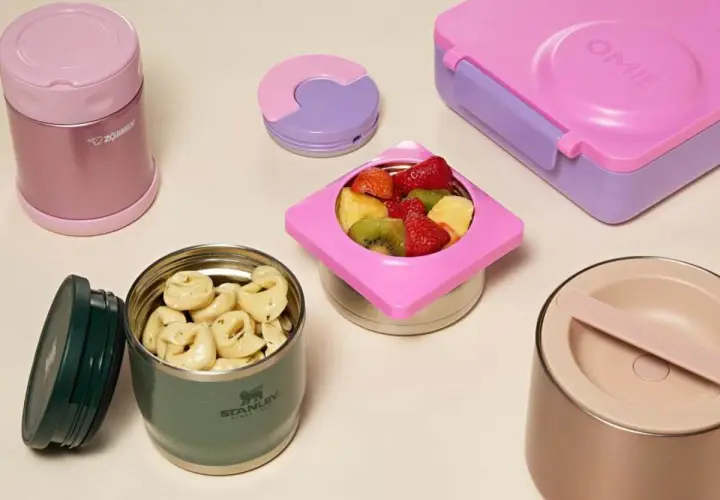 Colorful bento boxes and insulated food jars filled with pasta and fruit. These containers are designed to keep food warm for lunch.