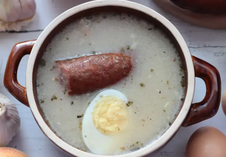 Aromaticzny żurek z kiełbasą i jajkiem, przygotowany na bazie domowego zakwasu na żurek. Obok czosnek, cebula i jajka.