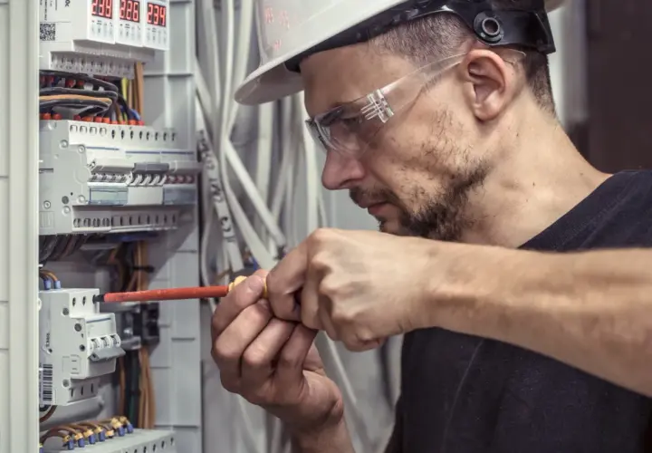 Technik elektryk w okularach ochronnych i kasku precyzyjnie dokręca śrubę w skrzynce rozdzielczej.