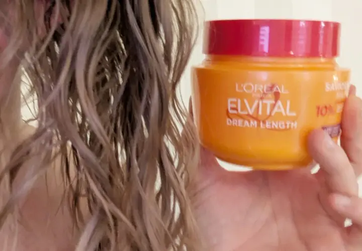 En hand håller en burk med L'Oréal Elvital Dream Length hårinpackning bredvid blekt, vått hår.