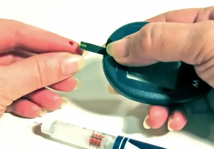 Kropla krwi na palcu, pasek testowy i glukometr. Obok wstrzykiwacz z insuliną aspart sanofi.