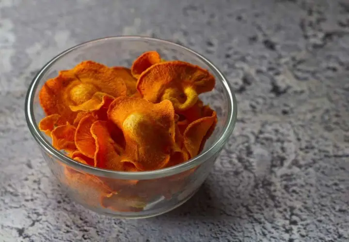 Croccanti chips di carote, preparate in friggitrice ad aria, servite in una ciotola di vetro.