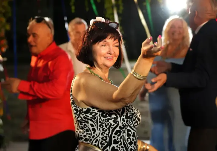 Uśmiechnięta kobieta w panterce tańczy na imprezie. W tle widać bawiących się ludzi, nie ma mocnych obsada, tylko radość.