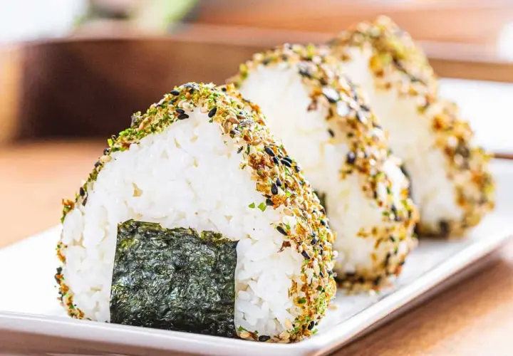 Triangular onigiri rice balls, coated in furikake seasoning, showcase the best rice for onigiri. A piece of nori seaweed adorns the front.