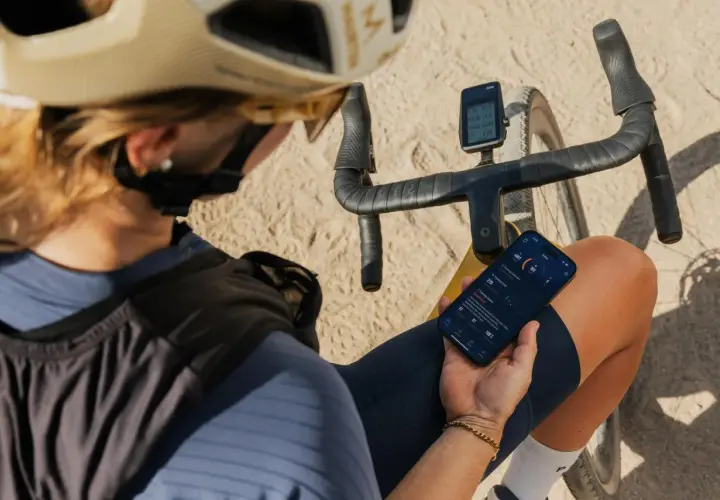 Jaka nawigacja na rower? Kolarz sprawdza dane treningowe na telefonie i liczniku rowerowym, planując dalszą trasę.