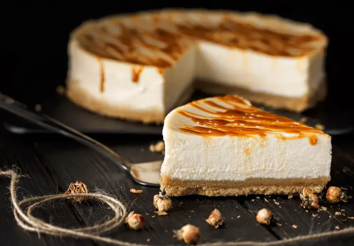 Una fetta di cheesecake fredda senza gelatina, con glassa al caramello, su un piatto scuro.
