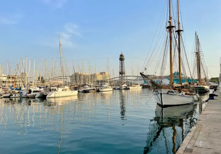 Port w Barcelonie z żaglówkami i wieżą widokową w tle.