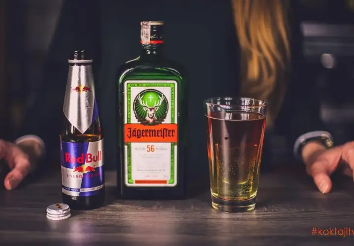 Butelka Red Bull i Jägermeister obok szklanki z drinkiem. Idealny zestaw na imprezę.