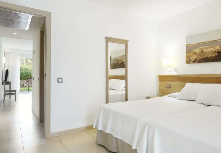 Habitación luminosa en Iberostar Club Cala Barca con dos camas, espejo de cuerpo entero y acceso a un patio exterior.