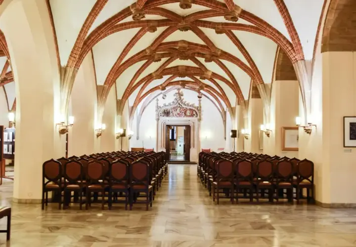 Wnętrze sali z rzędami krzeseł i ozdobnym sklepieniem.