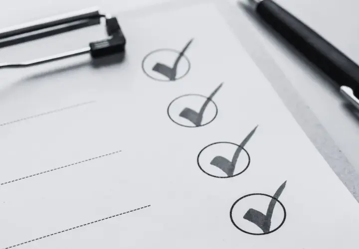 Liste de contrôle pour une visite maison : un stylo noir et un presse-papiers sur une feuille avec des cases cochées.