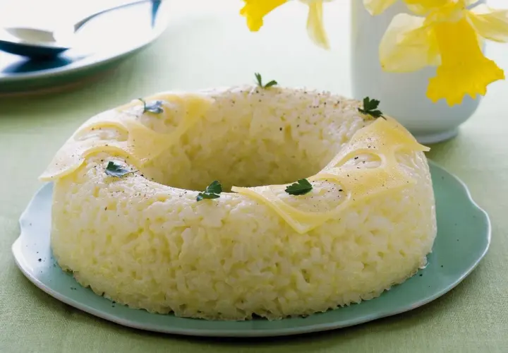 Sformato di riso a ciambella, decorato con fette di formaggio e prezzemolo, su un piatto verde.
