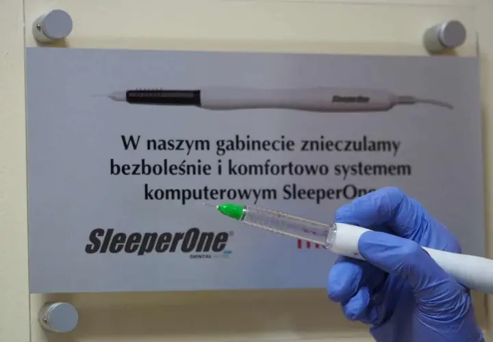 Ręka w niebieskiej rękawiczce trzyma aplikator z bupiwakainą, obok tablica informująca o bezbolesnym znieczuleniu komputerowym SleeperOne.