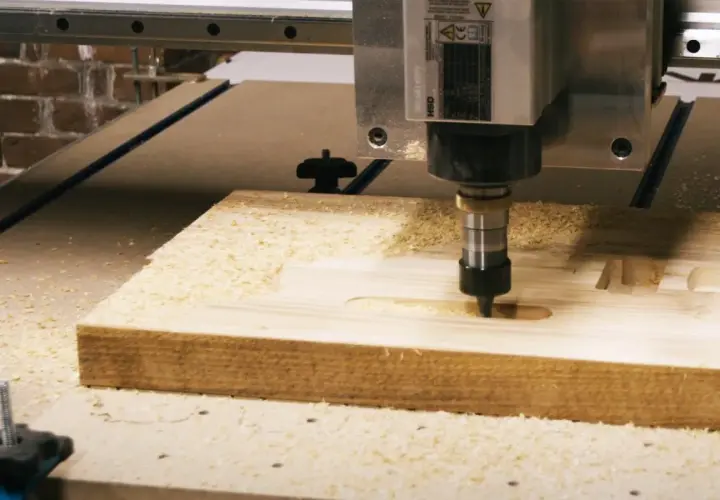 Precyzyjny frez CNC pracuje nad drewnianym elementem, tworząc rowki i kształty. Wióry drewna unoszą się wokół.