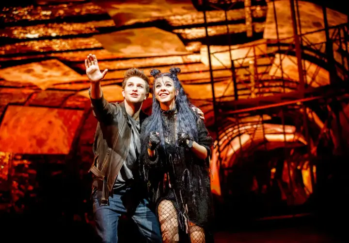 Para z musicalu "We Will Rock You" w polskim tłumaczeniu, pozdrawia publiczność na tle scenografii.