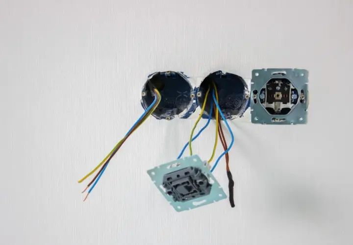 Instalacja elektryczna: puszki, przewody i mechanizmy gniazdek na białej ścianie.