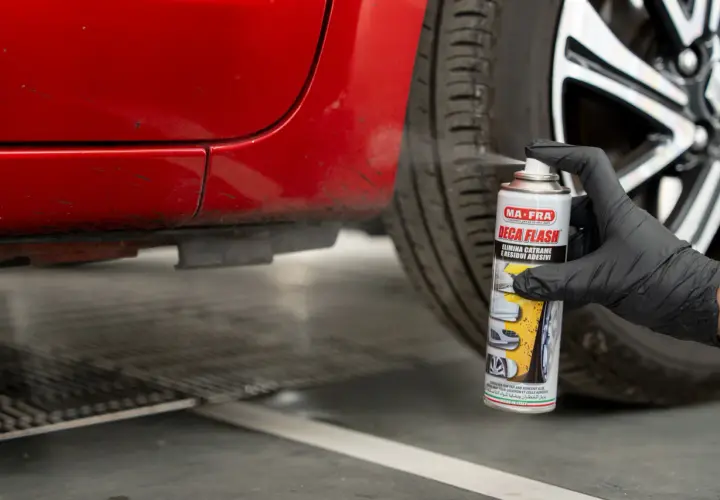 Guanto nero spruzza prodotto su auto rossa per togliere il catrame.
