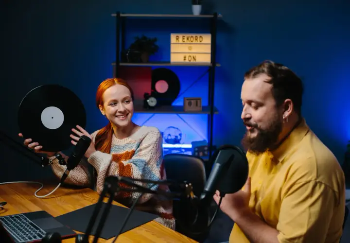 Coppia sorridente registra podcast in inglese interessanti, lei tiene un vinile, lui parla al microfono.