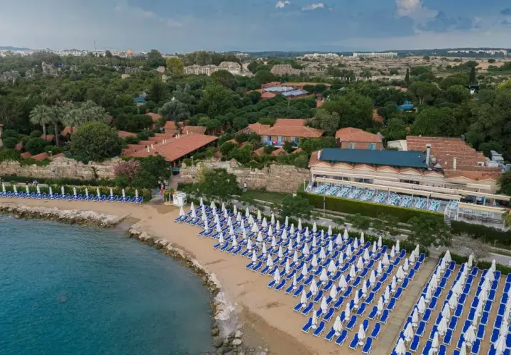 Piękna plaża z rzędami leżaków i parasoli, obok hotel z ogrodem i widokiem na morze. Idealne miejsce na wakacje.