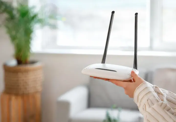 Dłoń trzyma biały router Wi-Fi z dwiema antenami. Może to być pomocne, gdy zastanawiasz się, jak zresetować urządzenie.