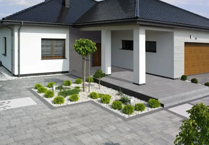 Nowoczesne projekty kostki brukowej wokół domu tworzą elegancką przestrzeń. Szara kostka, biały grys i zielona roślinność.