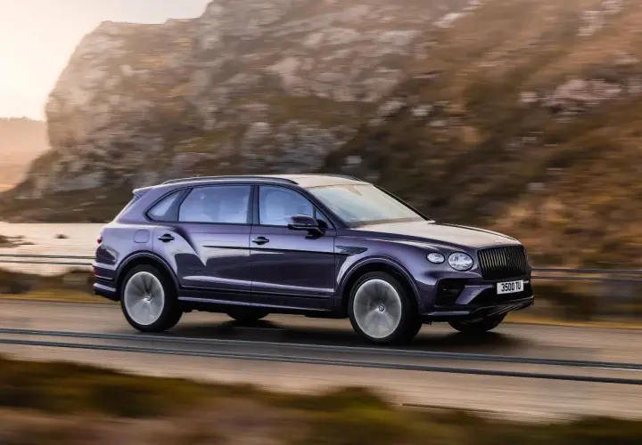 Fioletowy Bentley SUV pędzi po górskiej drodze, otoczony jesiennym krajobrazem.