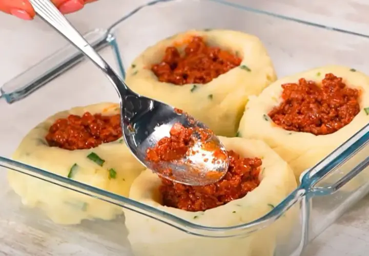 Łyżka nakłada mięsne nadzienie do ziemniaczanych łódeczek. Pyszne dania z ziemniaków w szklanym naczyniu.