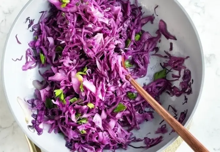 Insalata fresca di cavolo rosso, tagliato finemente e condito con erbe aromatiche, servita in una ciotola con un cucchiaio di legno.
