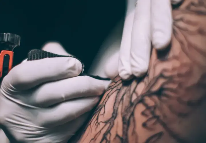 Dłoń w rękawiczce tworzy tatuaż metodą handpoke. To precyzyjne, ręczne tatuowanie, które daje unikalne efekty.
