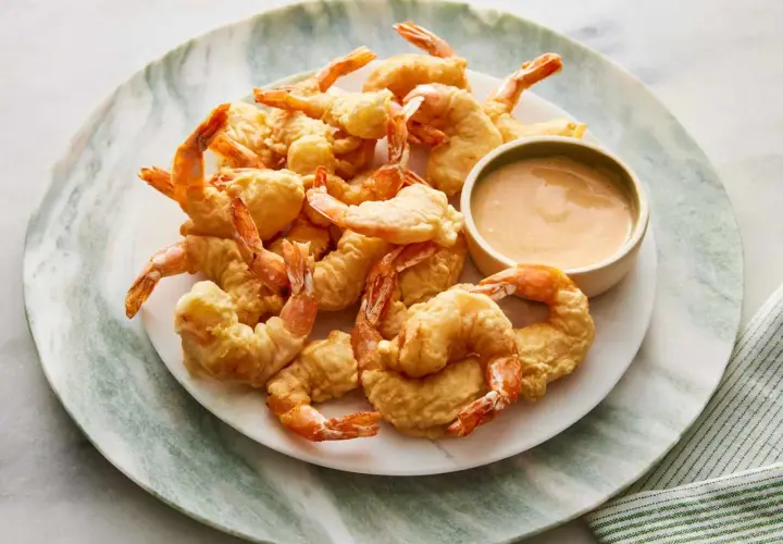 A plate piled high with golden-brown shrimp tempura, served with a small bowl of creamy dipping sauce.